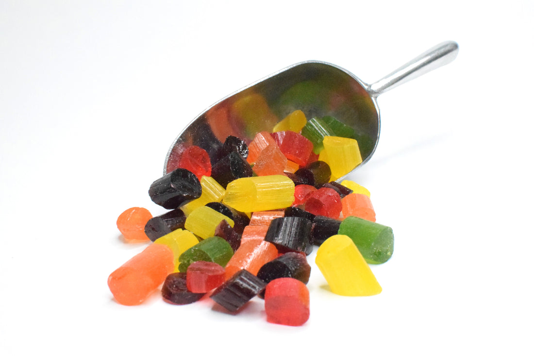 a small metal scoop on its side with multi coloured sweets piled around it. 